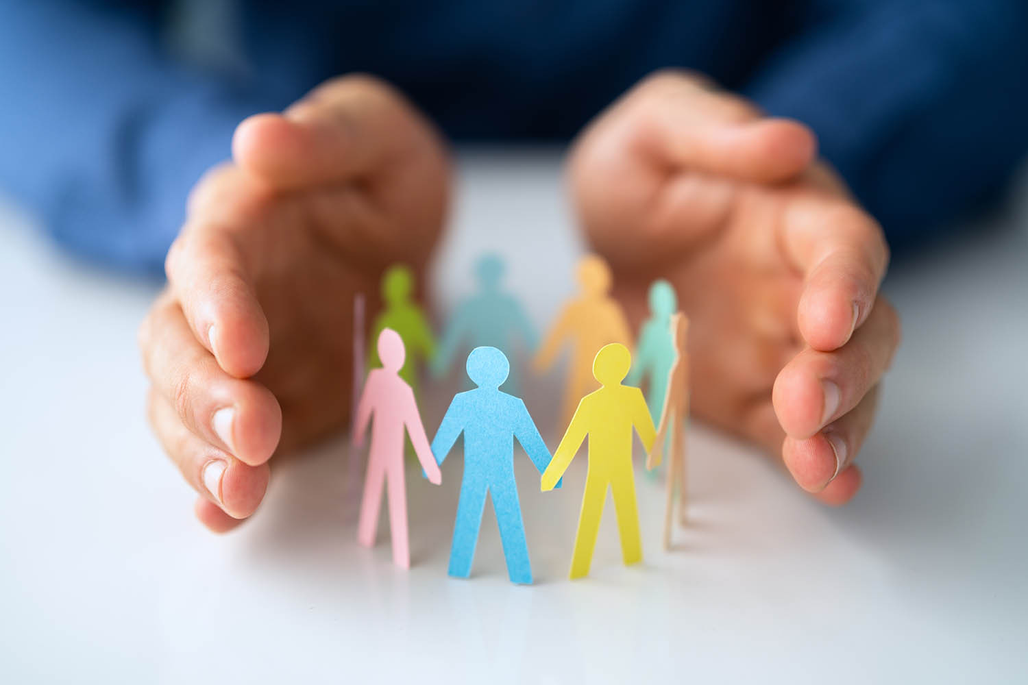 two hands that are encircling paper figures of people - to respresent adult safeguarding