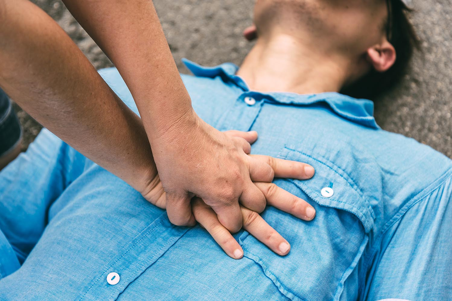 close up photograph of one hand clasped over another, performing CPR on a unconscious persons' chest